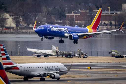 Aircraft land next to flatbed trucks carrying pieces of wreckage, near the site in the Potomac Rive…