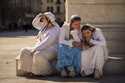 Women look at a phone while sitting on the pedestal of statue on International Women's Day in downt…