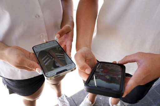 14-year-old Henry, right, and Angel, 15, use their phones to view social media in Sydney, Friday, N…