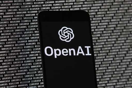 The OpenAI logo appears on a mobile phone in front of a computer screen with random binary data, Ma…