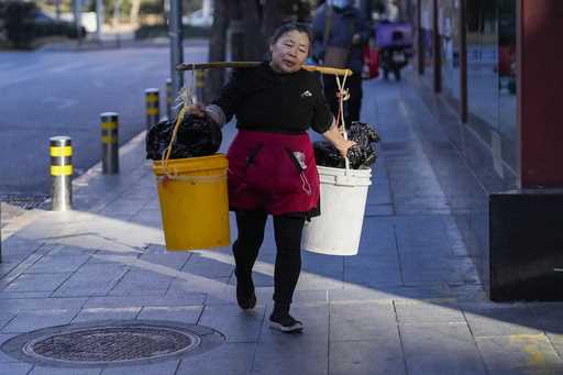 A woman carries two buckets along a street in the morning on Wednesday, January 8, 2025, in Beijing…