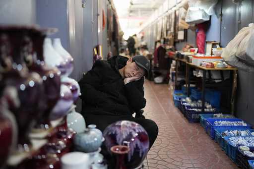 A vendor sleeps as he waits for customers at a market in Beijing, Thursday, January 16, 2025