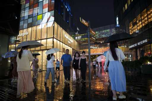 People walk under the rain with umbrellas at Taikoo Li Sanlitun in Beijing, Tuesday, July, 30, 2024…