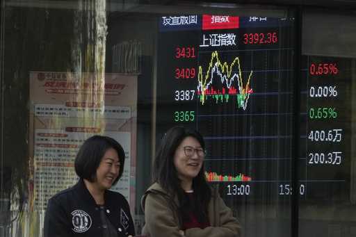 Women walk past by a display showing the Shanghai stock market index outside a brokerage in Beijing…