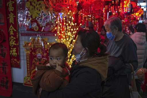 A woman carries a child as she shops at a New Year bazaar set up for the upcoming Chinese Lunar New…