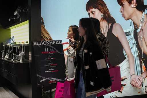 Women walk at a fashion accessories store displaying a poster to promote Singles' Day discounts at …