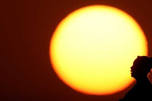 A woman is silhouetted against the setting sun as triple-digit heat indexes continue in the Midwest…