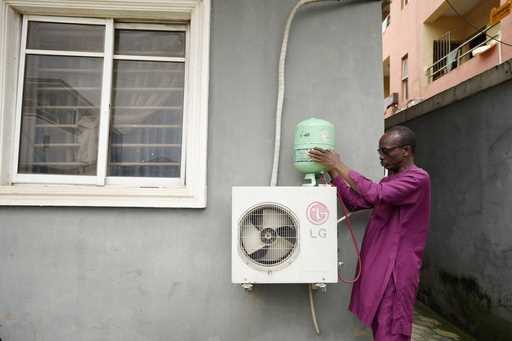 A technician positions an R-22 refrigerant on an outdoor air conditioning unit in Lagos, Nigeria, T…