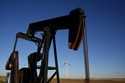 A pumpjack operates in the foreground as wind turbines at the Buckeye Wind Energy wind farm rise in…