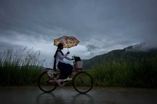 A school girl with an umbrella rides on her bicycle to school during a monsoon rain as clouds hover…