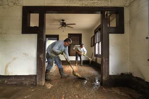 Ben Phillips, left, and his wife Becca Phillips scrape mud out of their living room in the aftermat…