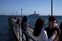 People walk at a dock with a drilling platform in the background, in the southern coastal city of L…