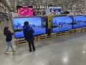 Young shoppers look over a row of large-screen televisions on display in a Costco warehouse Thursda…