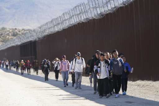 A group of people, including many from China, walk along the wall after crossing the border with Me…