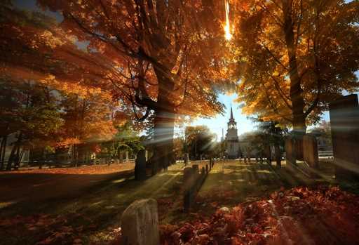 In this photo taken with a slow shutter speed, autumn's colors peak on hardwood trees in a cemetery…