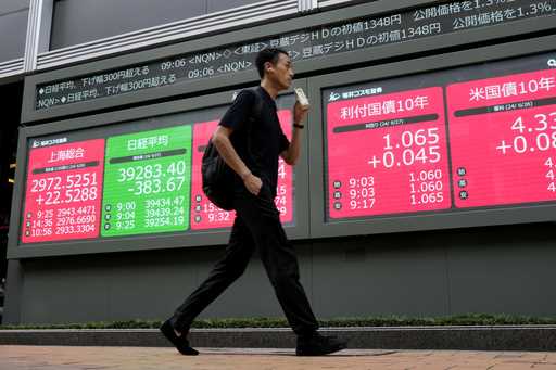 A person walks past at an electronic stock board showing financial indexes including Japan's Nikkei…