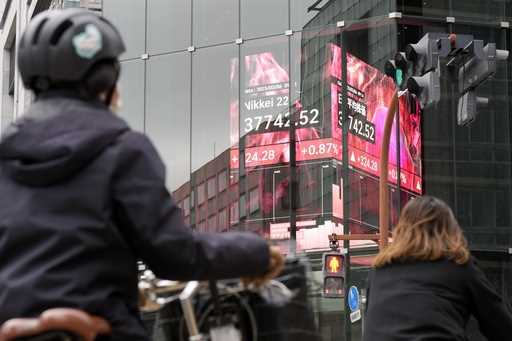 People stand in front of an electronic stock board showing Japan's Nikkei index at a securities fir…