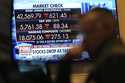 Financial news is displayed as people work on the floor at the New York Stock Exchange in New York,…