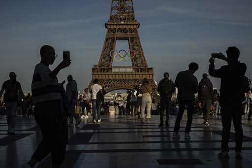 People use their smartphones near the Olympic rings that are displayed on the Eiffel Tower in Paris…