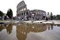 Tourists walk by the ancient Roman Colosseum as it's reflected in a puddle, in Rome, Sept