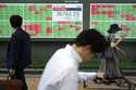 People walk in front of an electronic stock board showing Japan's Nikkei index at a securities firm…