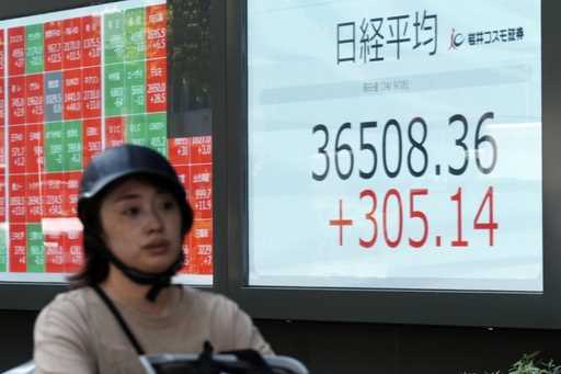 A person rides a bicycle in front of an electronic stock board showing Japan's Nikkei index at a se…