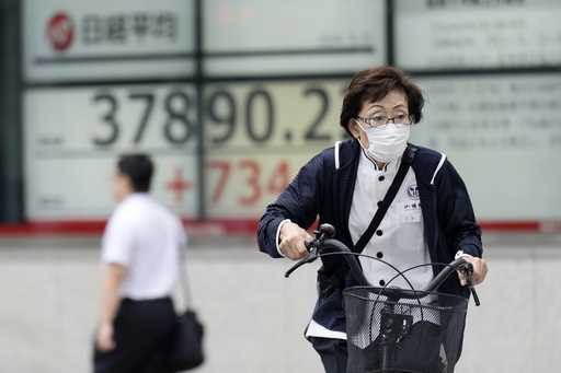 A person rides a bicycle in front of an electronic stock board showing Japan's Nikkei index at a se…