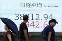 People walk in front of an electronic stock board showing Japan's Nikkei index at a securities firm…