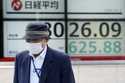 A person walks in front of an electronic stock board showing Japan's Nikkei index at a securities f…