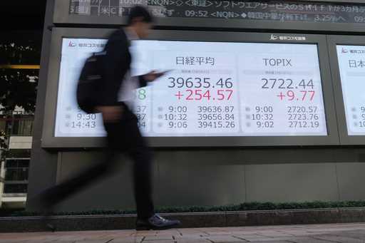 A passerby walks past an electronic stock board showing Japan's Nikkei 225 index, center, in front …