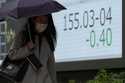 A woman walks by a monitor showing Japan's foreign exchange rate against the U