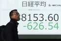 A person walks in front of an electronic stock board showing part of Japan's Nikkei index at a secu…