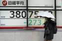 A person walks in front of an electronic stock board showing Japan's Nikkei index at a securities f…