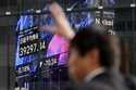 A person gestures in front of an electronic stock board showing Japan's Nikkei index at a securitie…