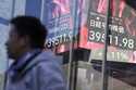 People stand in front of an electronic stock board showing Japan's Nikkei index at a securities fir…