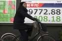 A person rides a bicycle in front of an electronic stock board showing Japan's Nikkei index at a se…