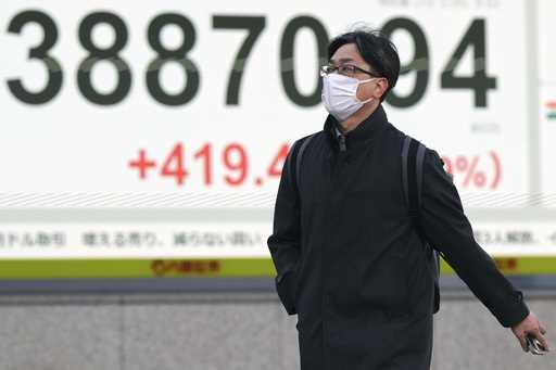 A person walks in front of an electronic stock board showing Japan's Nikkei index at a securities f…