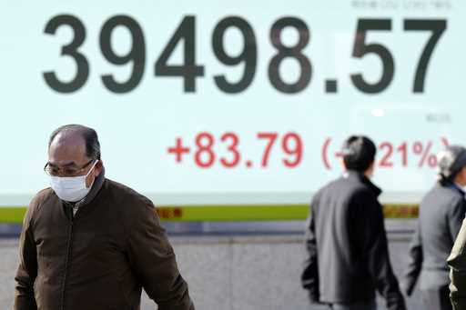 People walk in front of an electronic stock board showing Japan's Nikkei index at a securities firm…