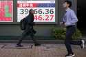 People walk in front of an electronic stock board showing Japan's Nikkei index at a securities firm…