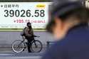 A person riding a bicycle waits in front of an electronic stock board showing Japan's Nikkei index …