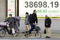 People stand in front of an electronic stock board showing Japan's Nikkei index at a securities fir…