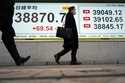 People walk in front of an electronic stock board showing Japan's Nikkei index at a securities firm…