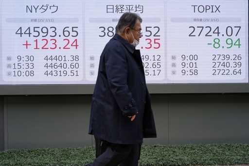 People walk in front of an electronic stock board showing Japan's Nikkei index at a securities firm…