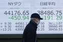 A person walks in front of an electronic stock board showing New York Dow, left, and Japan's Nikkei…