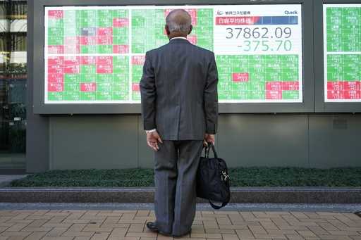 Persons walk past an electronic stock board showing Japan's Nikkei index at a securities firm Wedne…