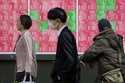 People walk in front of an electronic stock board showing Japan's Nikkei index at a securities firm…