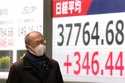 A person walks in front of an electronic stock board showing Japan's Nikkei index at a securities f…