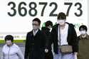 People walk in front of an electronic stock board showing Japan's Nikkei index at a securities firm…