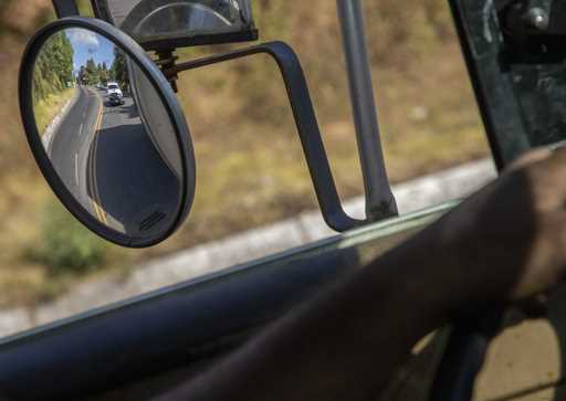 Trucks loaded with avocados are seen reflected on a rear view mirror as they are escorted by the po…