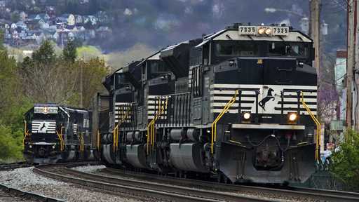 A Norfolk Southern freight train passes a train on a siding as it approaches a crossing in Homestea…